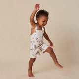 A toddler girl posing in a white halter romper with a colorful pirate-themed print, set against a solid beige studio background.