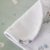 Rolled-up white towel on a green fabric background with floral patterns