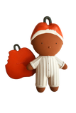 A stylized terracotta-colored doll character wearing a white striped onesie and an orange-and-white Santa hat, holding a red apple-shaped accessory with a black loop, shown on a plain white background.