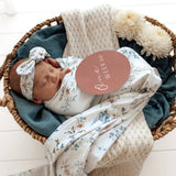 Newborn baby wrapped in floral blanket with 'one week old' tag in a basket