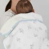 Person holding a baby wrapped in a white blanket with gray elephant patterns on a plain background