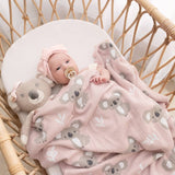Baby wrapped in a pink blanket with koala patterns, lying in a wicker crib.