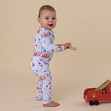 Baby in pajamas with vehicle pattern standing next to a wooden toy truck on a beige background