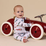 Baby sitting in a red toy car against a beige background