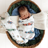 Newborn baby swaddled in a blanket with car patterns, lying in a woven basket.
