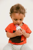 Child in an orange shirt holding a baby bottle against a white background