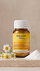 A bottle of Weleda Baby Teething Powder oral powder medicine, styled with chamomile flowers and a pile of white powder on a stone slab against a neutral beige background.