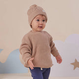 Baby wearing a brown knit sweater and beanie standing against a neutral background