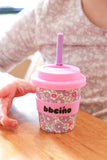 Pink floral-patterned cup with a straw on a wooden surface