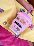 Pink cup with cartoon character and 'bbeino' branding held by a child in a yellow outfit.