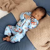 Newborn baby sleeping in a blue crib with a fire truck patterned onesie.