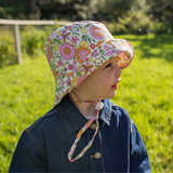 Child wearing a floral sun hat and denim jacket in a grassy outdoor setting