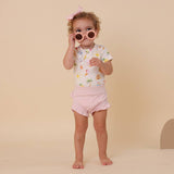 Child wearing a patterned shirt and pink shorts with sunglasses on a beige background