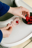 Person filling a pink container with raspberries from a bowl on a white surface.