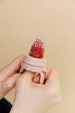 Hand holding a pink silicone product with a strawberry on a beige background