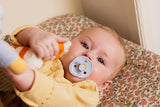 Baby in a yellow outfit with a pacifier, lying on a floral blanket.