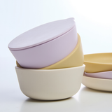 Set of three ceramic bowls with lids in pastel colors on a light background