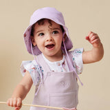 A baby wearing a lavender sun hat with a floral pattern and matching lavender bib over a white floral shirt, posed against a solid beige background.
