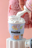 Ice cream cup with cartoon characters and 'bbeiáno' branding, being topped with whipped cream.
