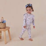Child wearing a floral onesie standing next to a wooden stool with a basket on a beige background