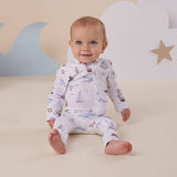 Baby wearing a patterned onesie sitting on a soft surface with a star and cloud decoration in the background.