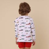 Child wearing a long-sleeve shirt with car pattern and red shorts on a beige background