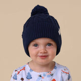Child wearing a navy blue knit hat with a pom-pom on a beige background