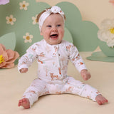 Baby wearing a floral outfit with a headband, sitting on a beige surface with a floral background.