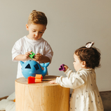 Two children playing with toys on a wooden table against a plain background