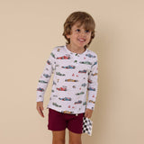 Child wearing a long-sleeve shirt with car pattern and maroon shorts on a beige background