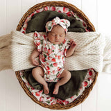 Newborn baby in a floral outfit and headband lying on a textured blanket inside a woven basket.