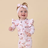 Baby wearing a floral onesie and headband on a beige background