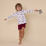 Child wearing a long-sleeve shirt with car print and maroon shorts, holding a checkered flag against a beige background.