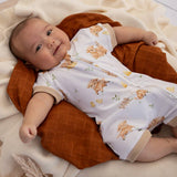 A baby lying on a quilted brown baby lounger, wearing a white short-sleeve romper with a brown animal print and beige trim.