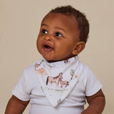A baby wearing a white short-sleeve bodysuit and a matching white bib with a printed design of horses and cacti, posed against a solid beige background.