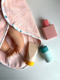 Baby lotion, bottle, and towel with a baby doll on a light gray background