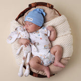 Newborn baby in a basket with a blue hat and patterned outfit, holding a soft toy.