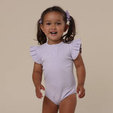 Child wearing a light purple onesie with ruffled sleeves against a beige background