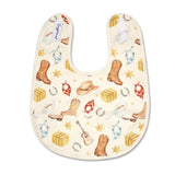 A cream-colored baby bib featuring a western-themed print with brown cowboy boots, a tan cowboy hat, red bandanas, yellow sheriff's badges, silver horseshoes, and yellow sheriff's badges, shown on a plain white background.
