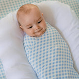 Baby swaddled in a blue and white checkered blanket on a white pillow with a blue checkered background.