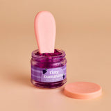 Jar of purple jelly with a pink spoon on a beige background