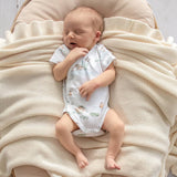 Newborn baby in a floral onesie lying on a soft beige blanket