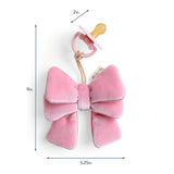 Pink plush bow with a pacifier attached, shown with measurements on a white background