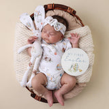 Baby in a basket with bunny ears, plush toy, and 'My First Easter' sign on a beige background