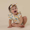 Baby wearing a lemon-patterned outfit and headband on a beige background