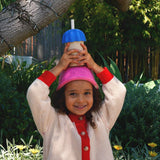 Child holding a colorful cup above their head in a garden setting
