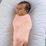 Newborn baby wrapped in a pink swaddle on a white cushion