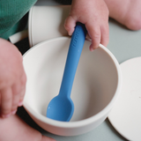 Baby holding a blue spoon over a white bowl