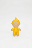 A small stylized doll figure with a yellow hood and matching yellow outfit, standing against a plain light gray background.