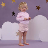 Child in pink outfit standing against a purple wall with star decorations